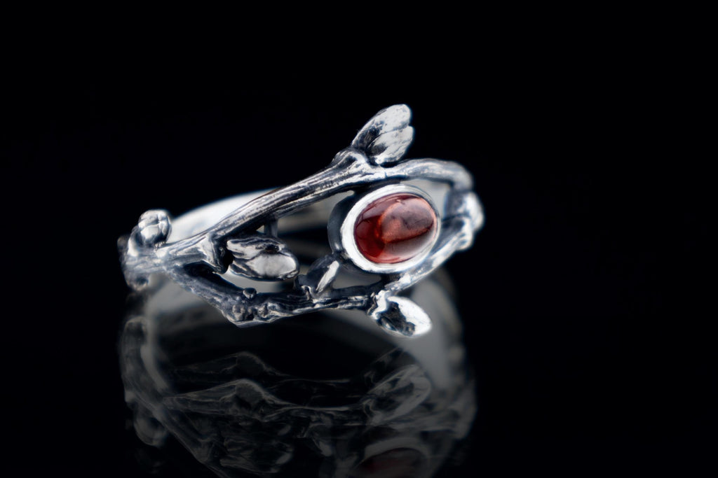 Botanical silver twig ring with natural garnet on dark background