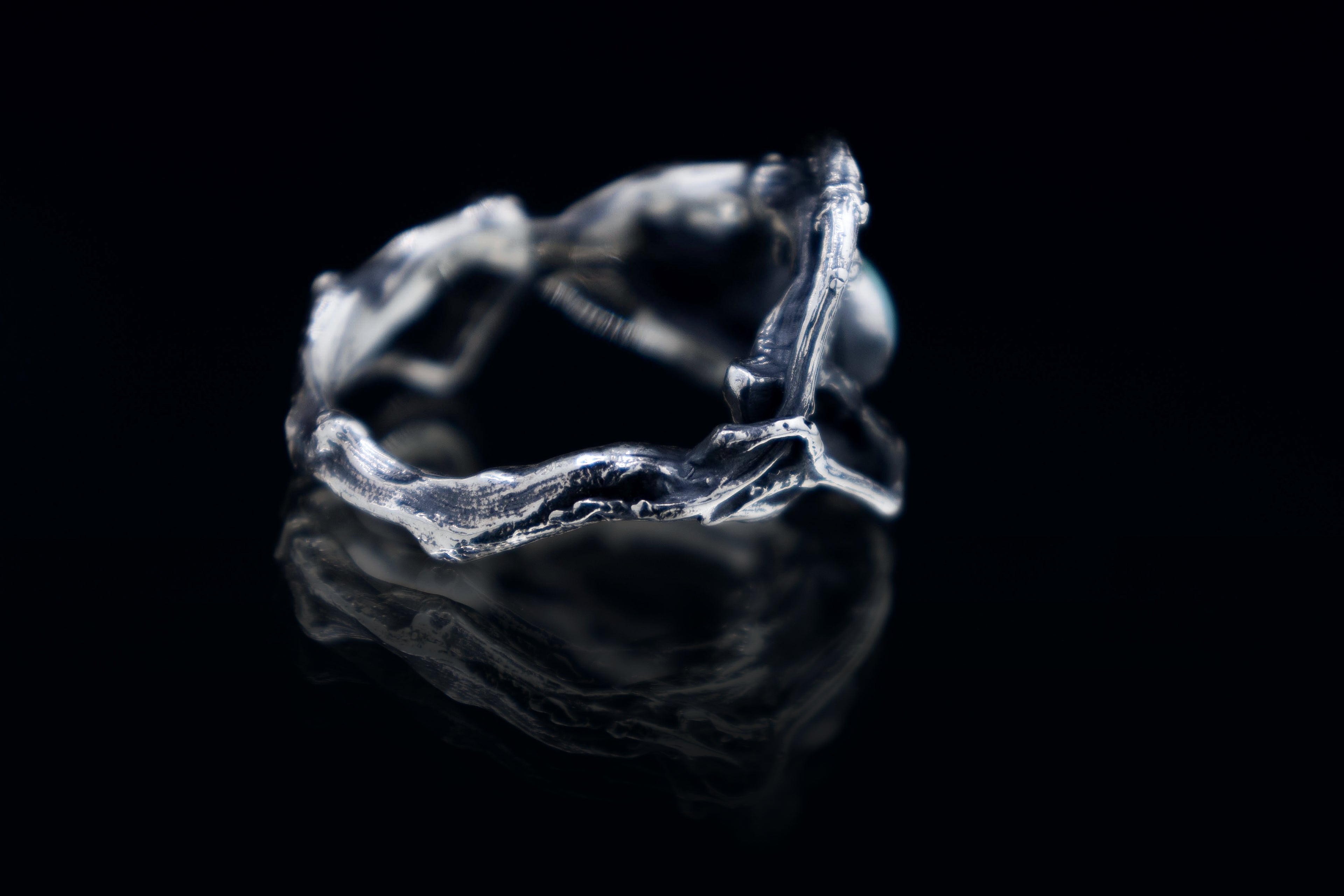Side/back angle of sterling silver roots ring with branch texture, oxidized finish, black background studio photo.