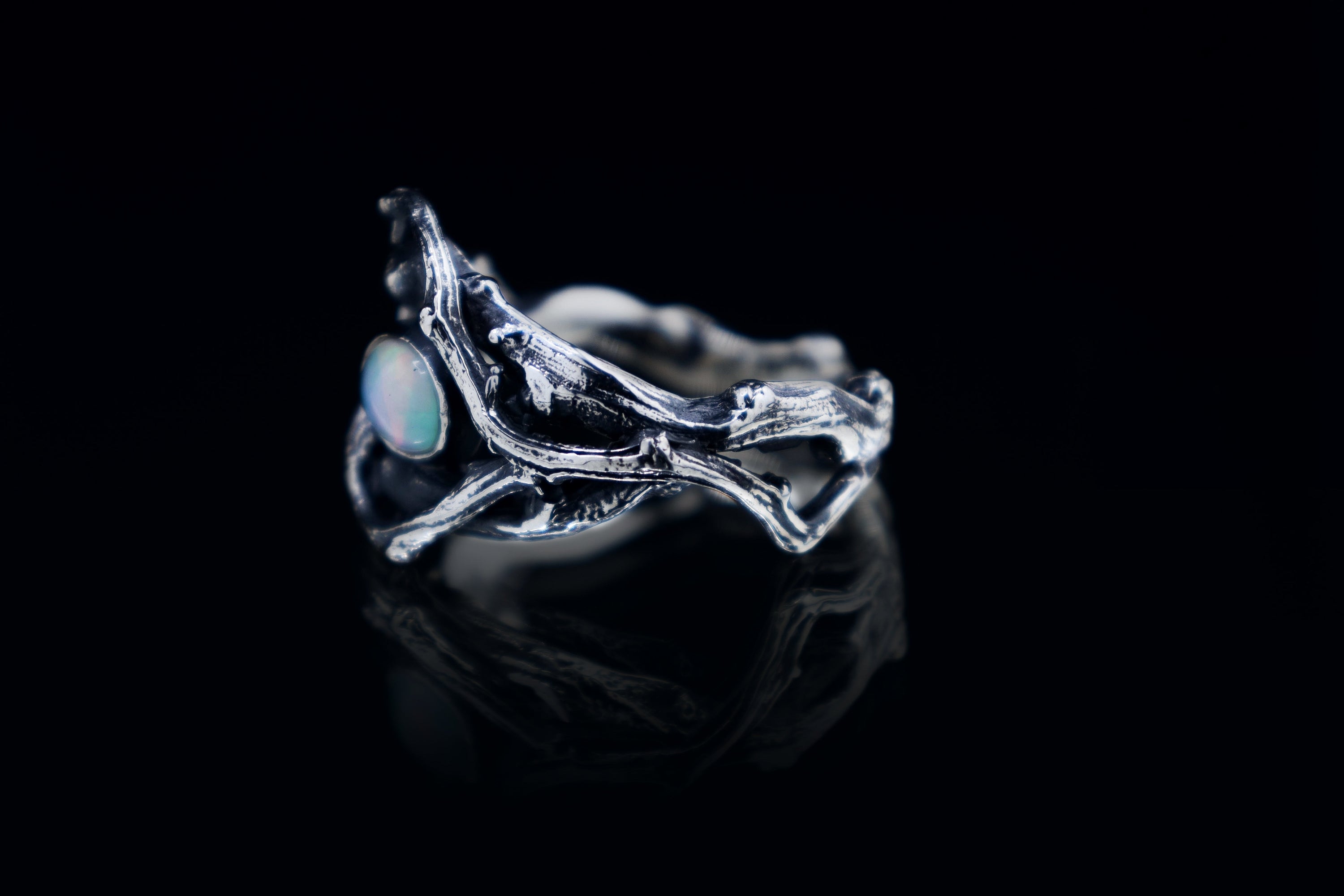 Sterling silver oxidized branch ring with Ethiopian opal cabochon, close-up on black background