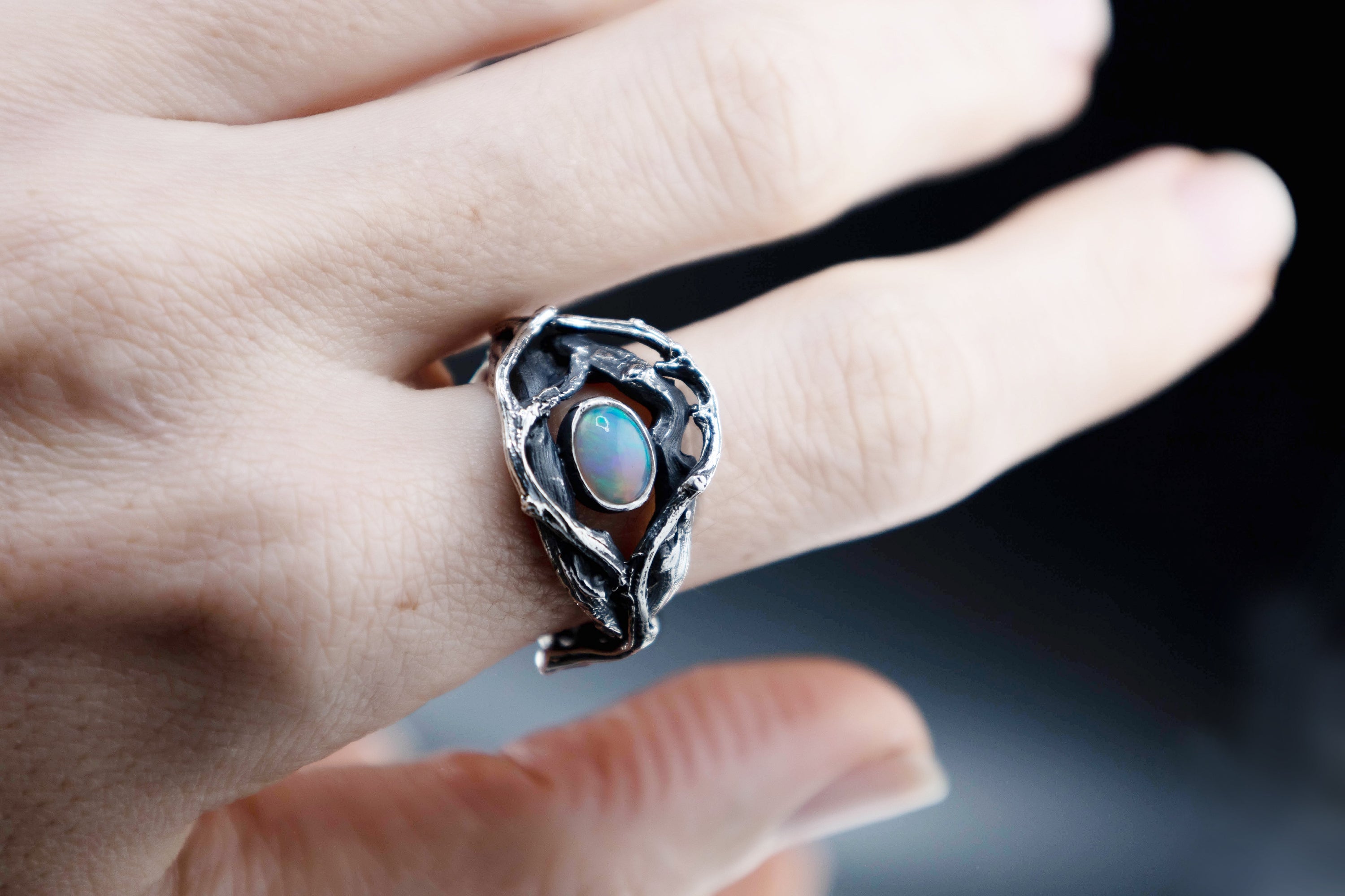 Sterling silver twig ring with 7x5mm Ethiopian opal on hand, organic roots design, top view for scale.