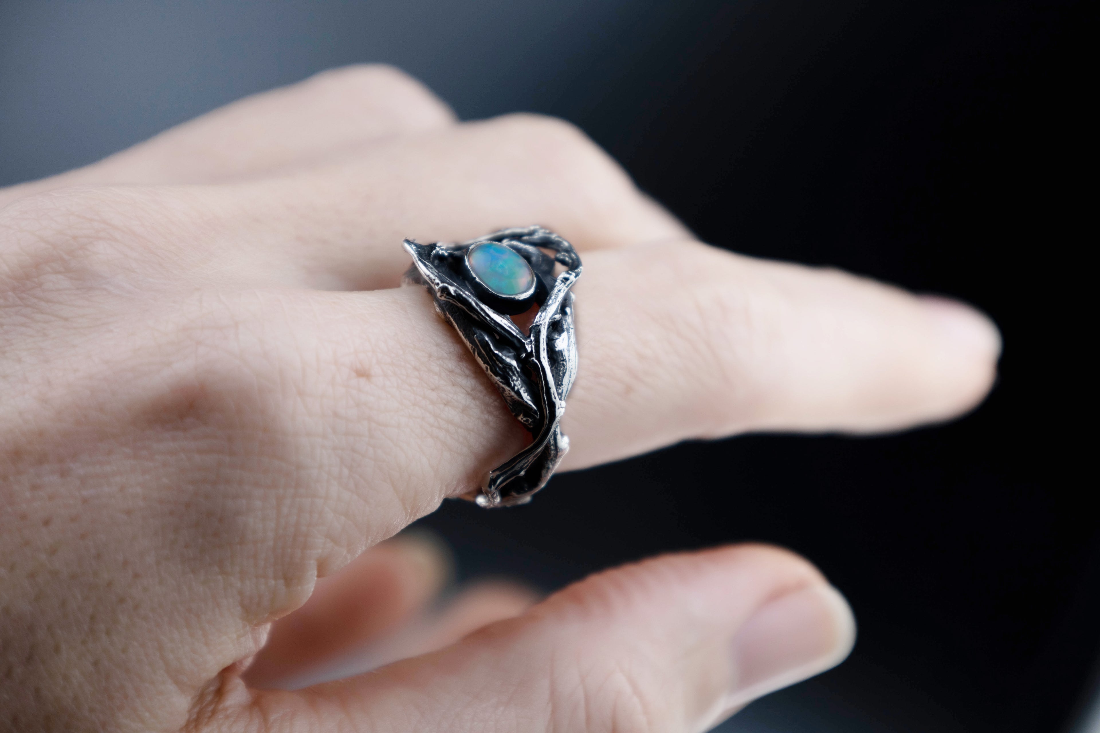 Sterling silver branch ring with Ethiopian opal worn on finger, oxidized finish, natural twig texture, side angle.