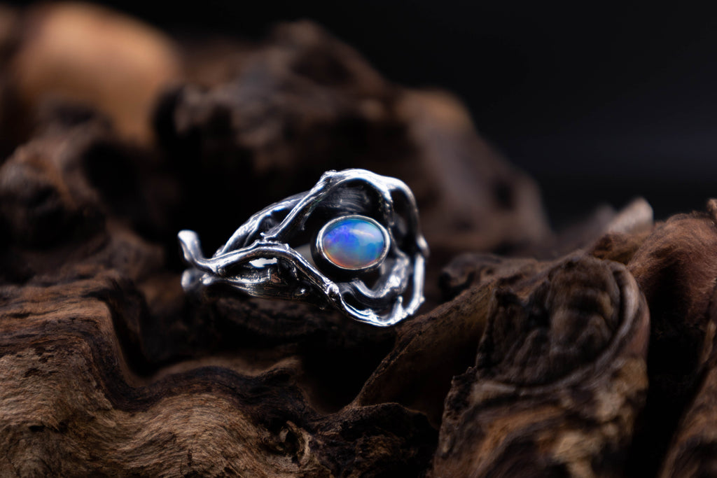 Sterling silver twig and root ring with Ethiopian opal cabochon on dark wood, woodland style, front view.