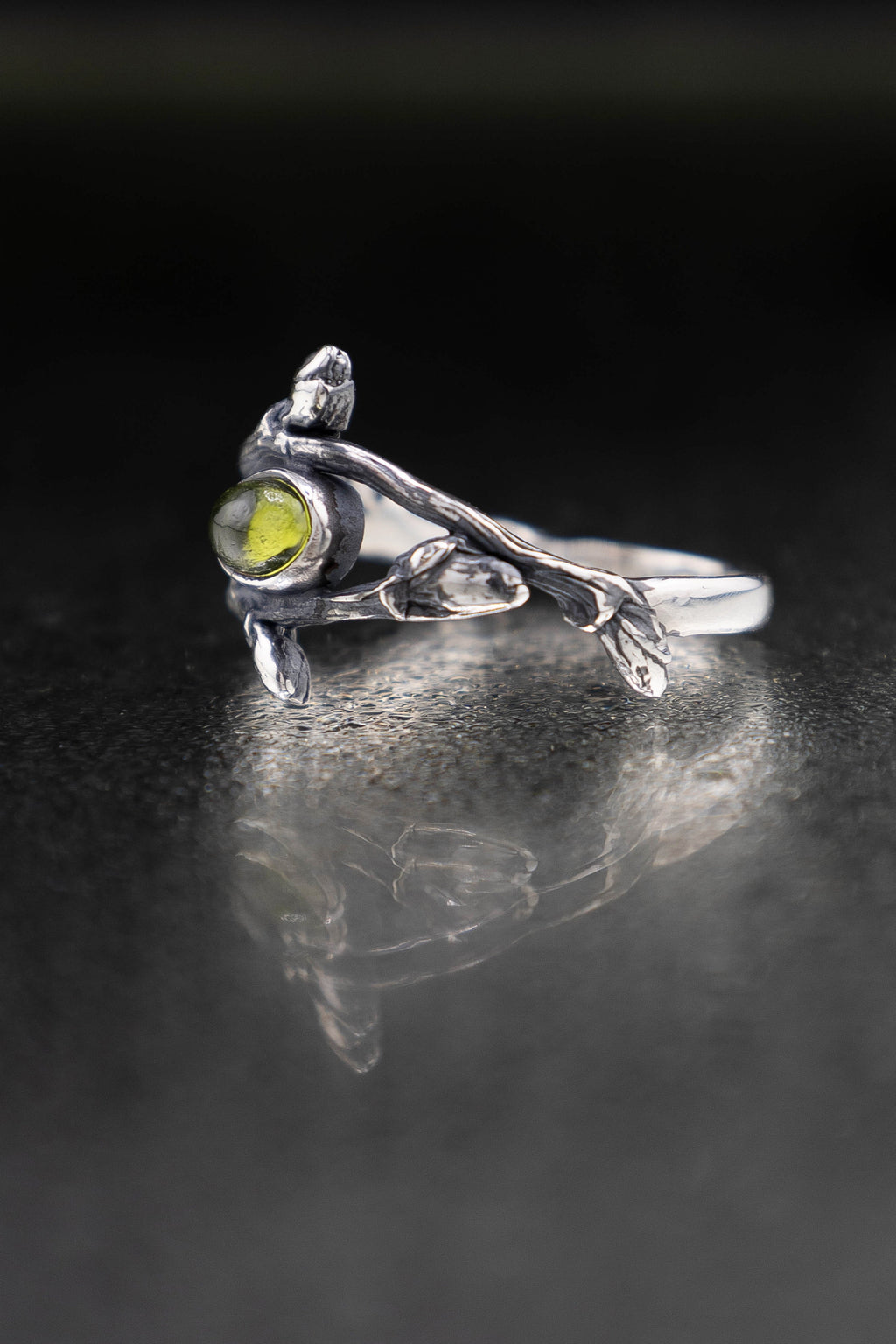 Silver ring with a green gemstone on a reflective black surface