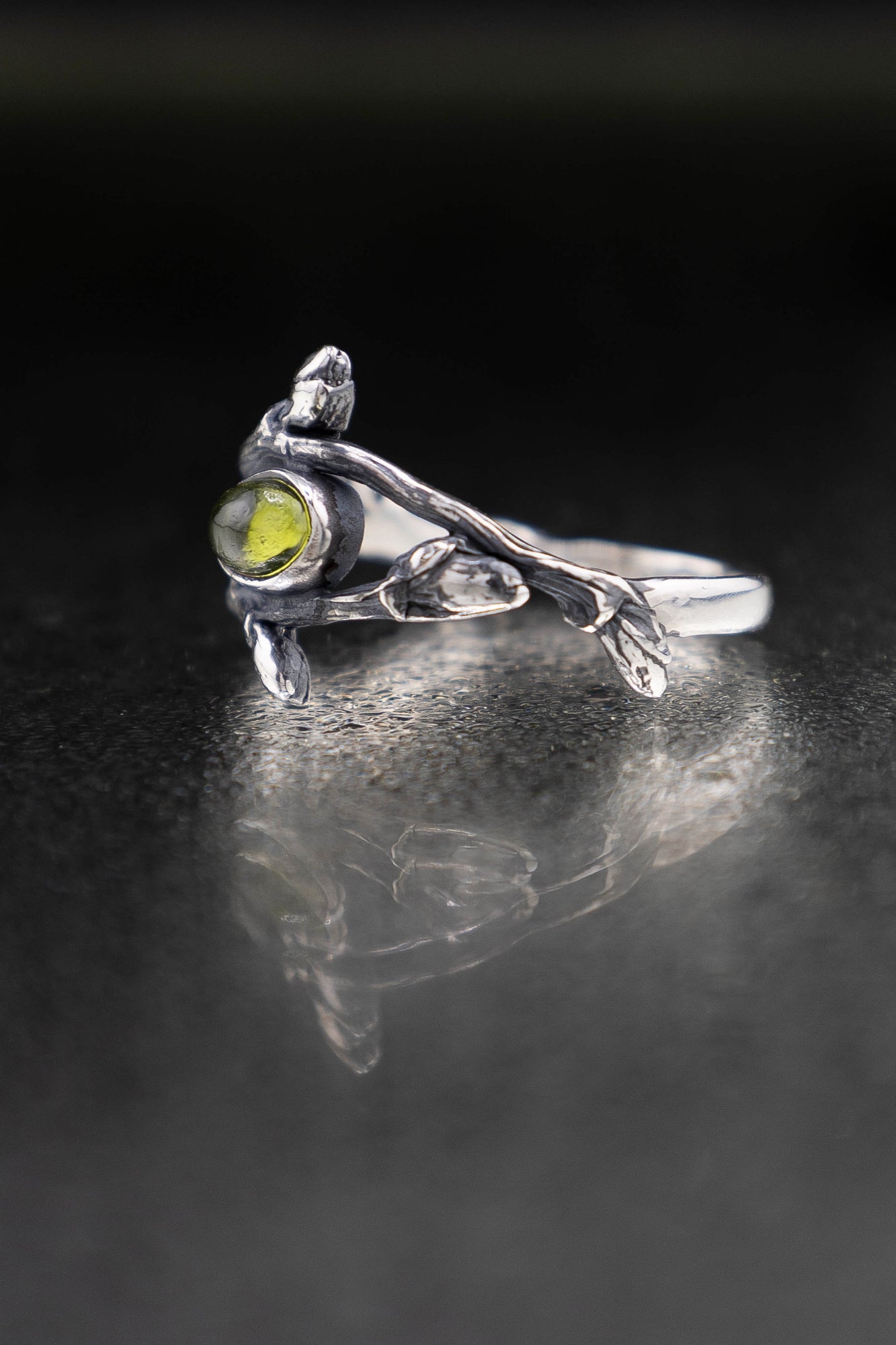 Silver ring with a green gemstone on a reflective black surface