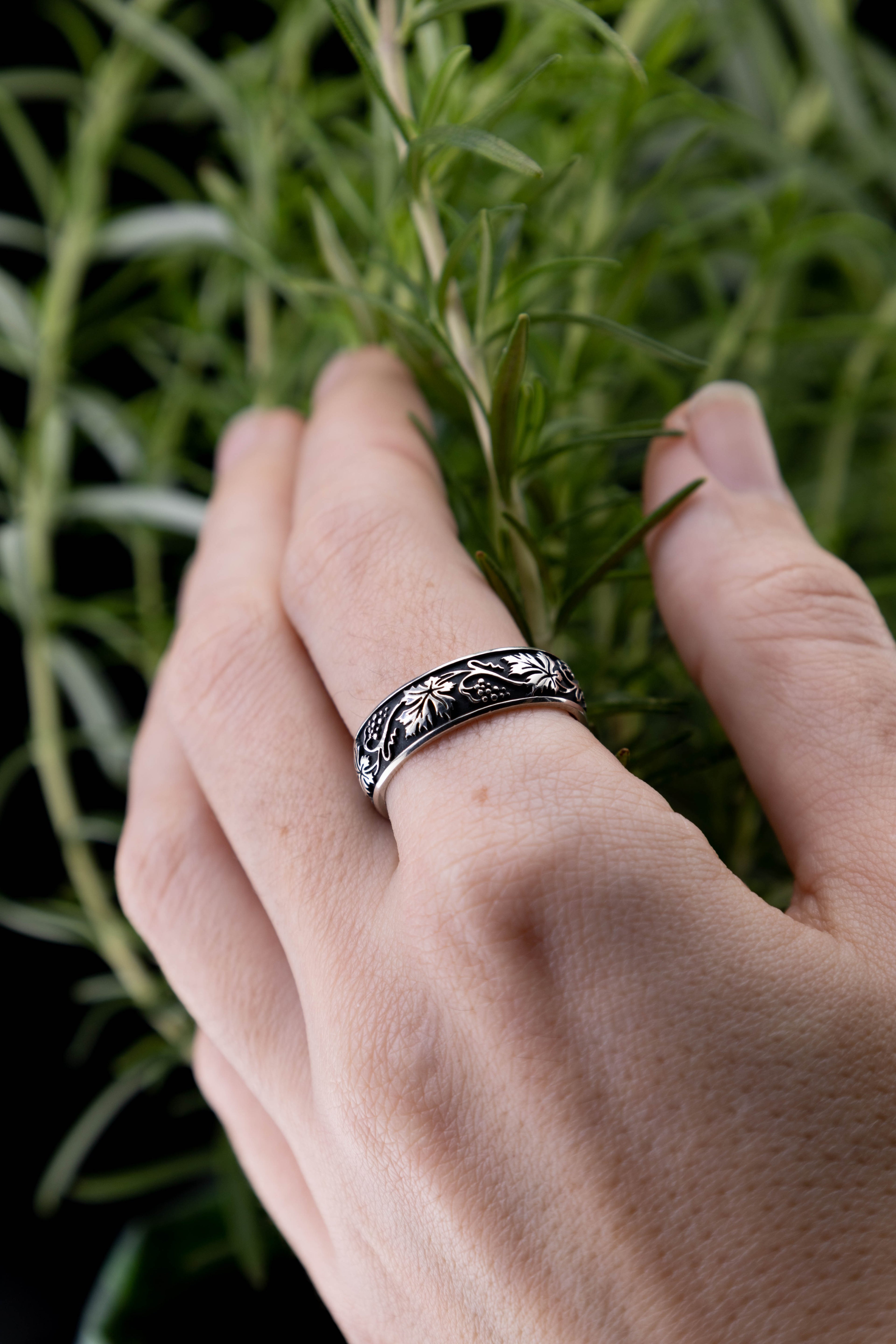 Sterling silver grape leaf ring with intricate berry pattern, botanical wedding band reflecting on glass surface, handcrafted nature jewelry artifact.