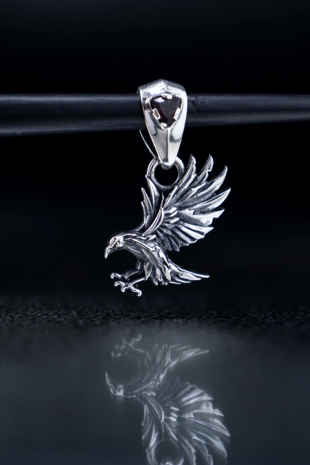 Sterling silver raven pendants on black reflective glass, gothic crow necklaces with blue or red gemstone bails, mythical bird jewelry artifact.