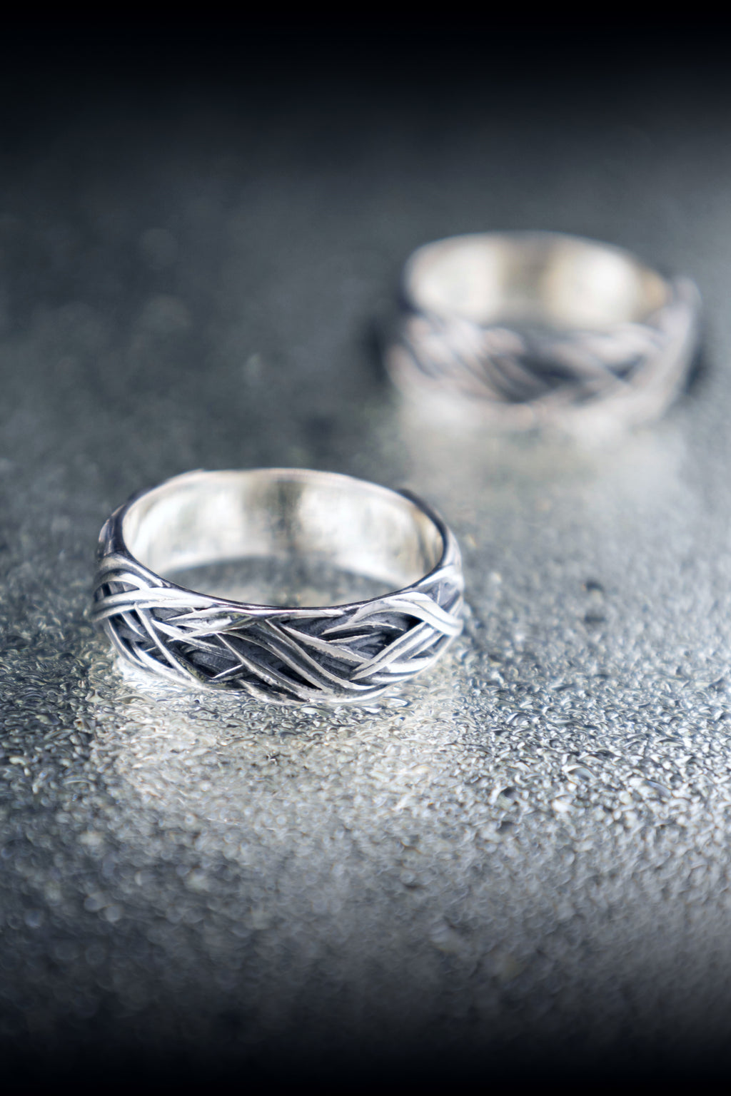 Two silver rings with textured band design on a dark surface