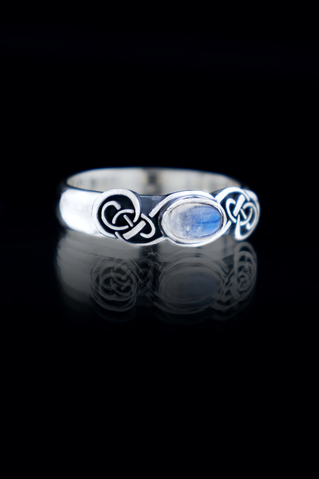Handmade sterling silver Celtic knot ring with natural Moonstone cabochon, oxidized knotwork band, on black reflective surface