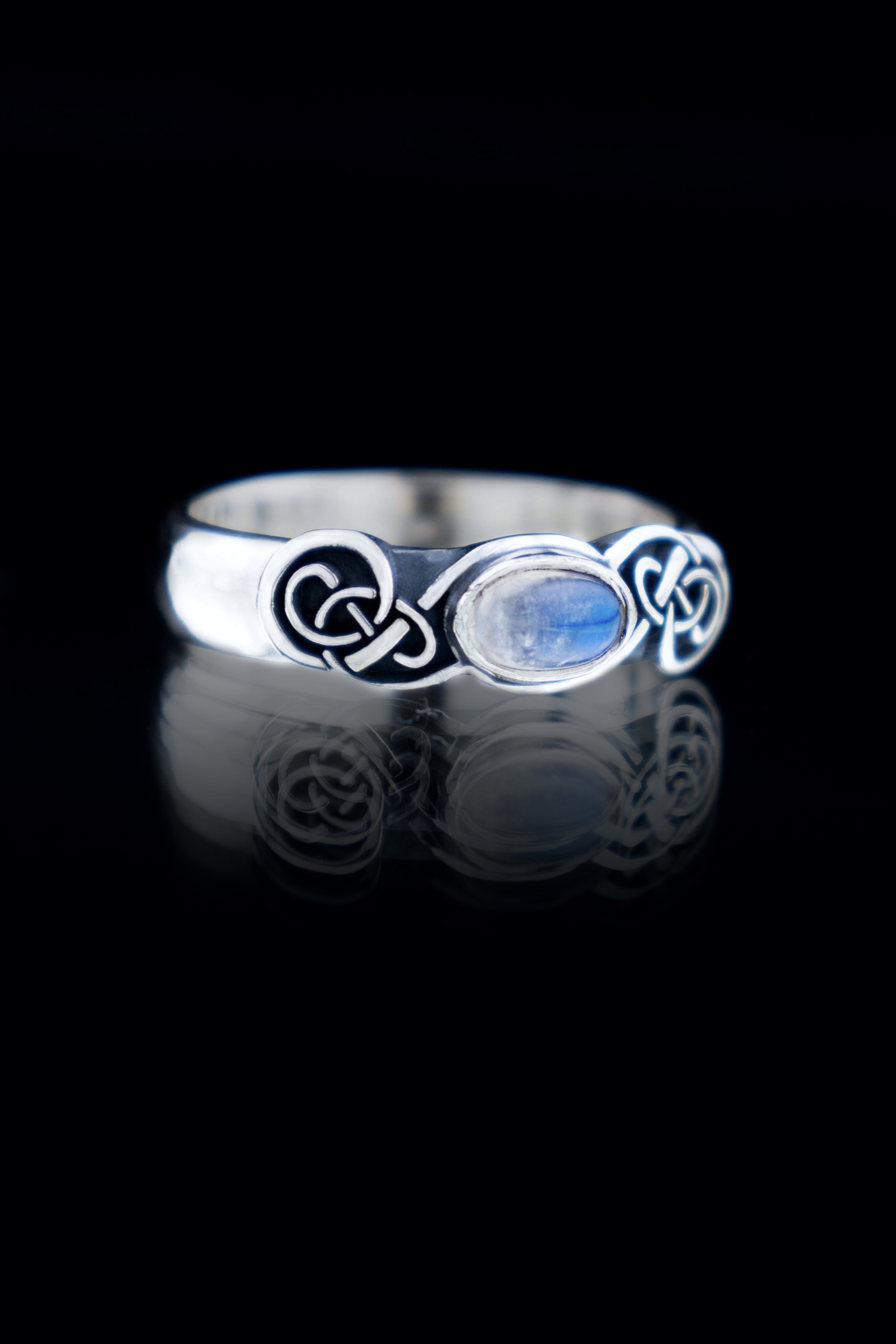 Handmade sterling silver Celtic knot ring with natural Moonstone cabochon, oxidized knotwork band, on black reflective surface