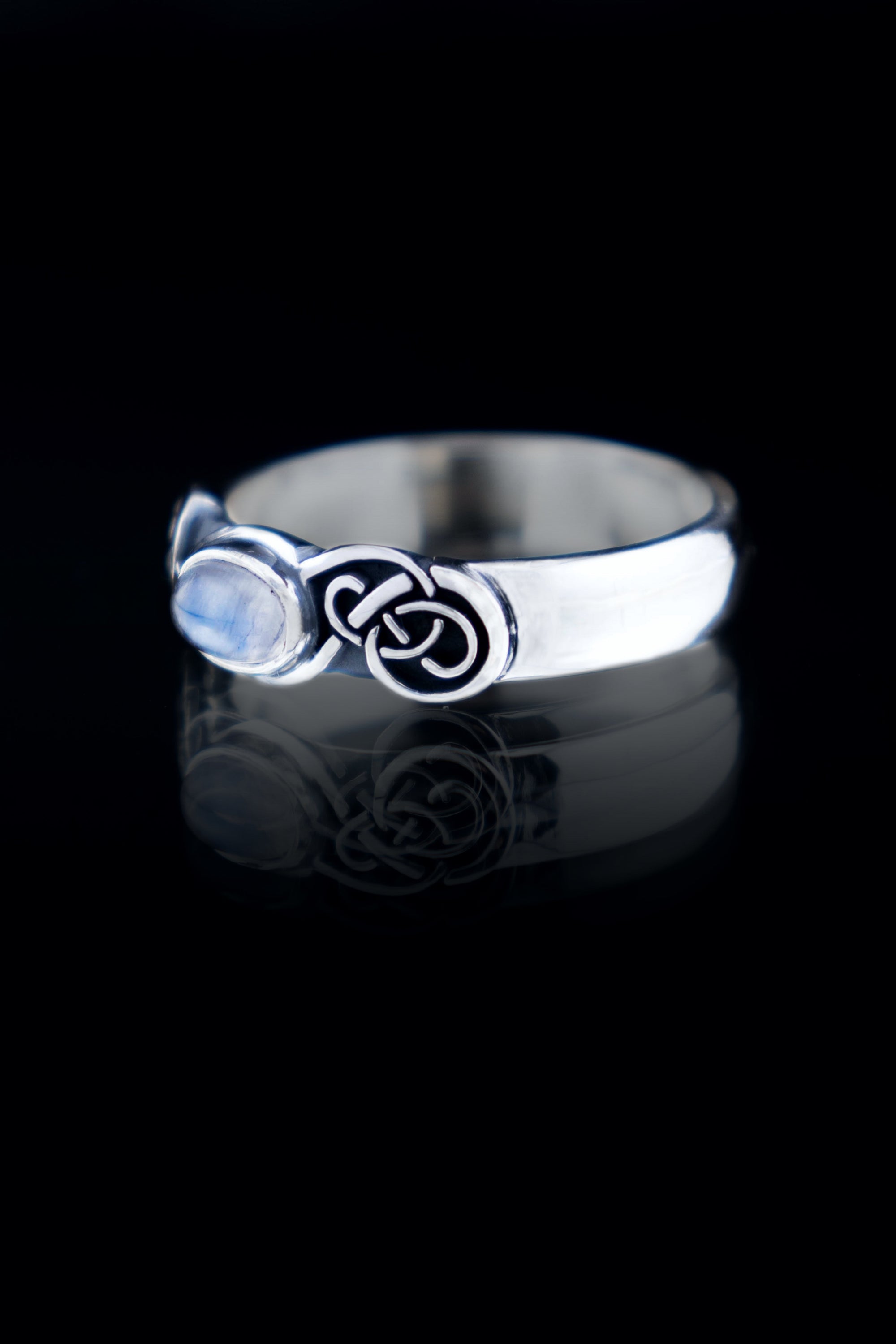 Handmade sterling silver Celtic knot ring with natural Moonstone cabochon, oxidized knotwork band, on black reflective surface