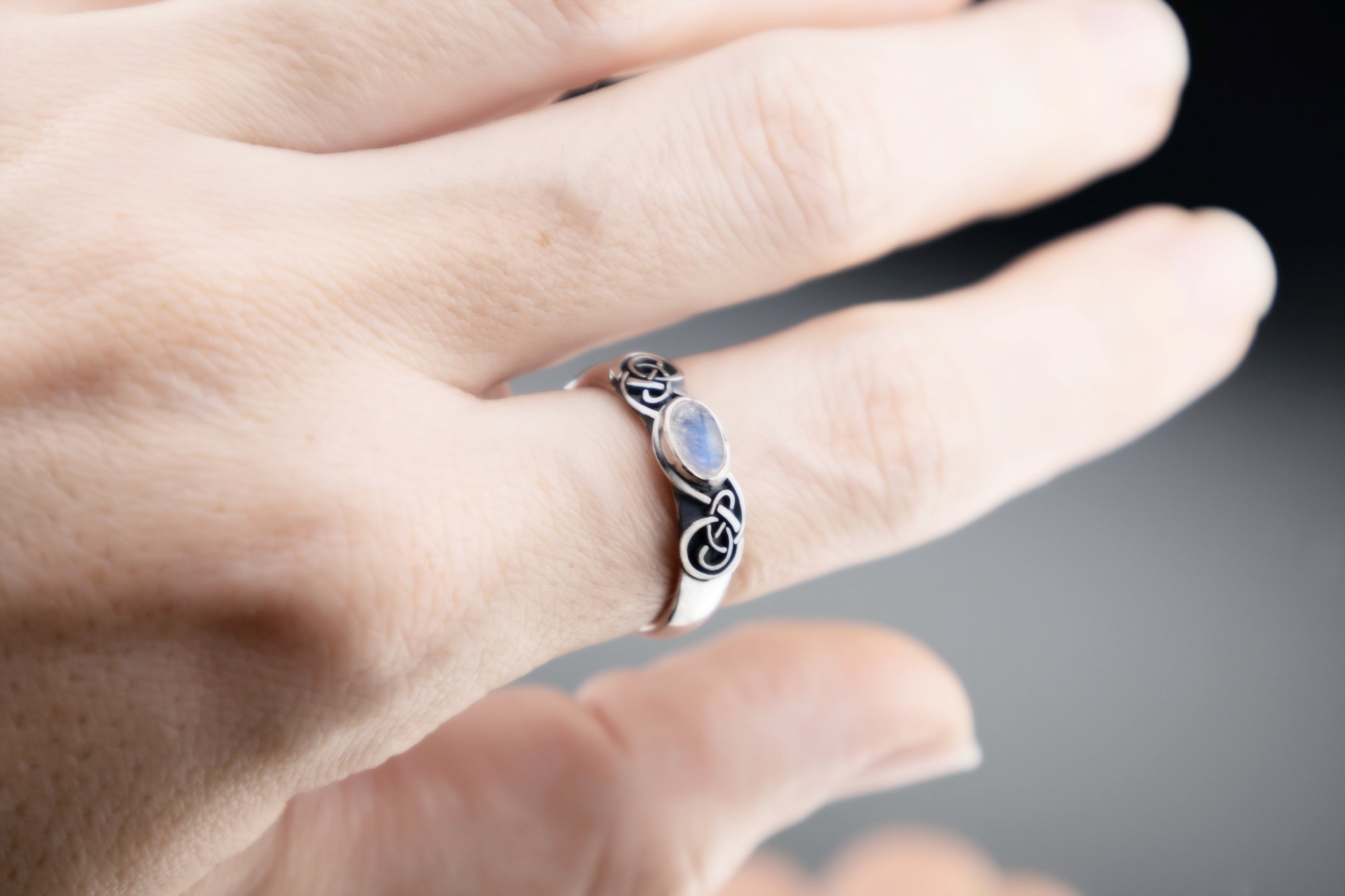 Sterling silver Celtic knot ring with blue Moonstone, oxidized symmetrical knotwork pattern, handmade pagan jewelry on stone surface