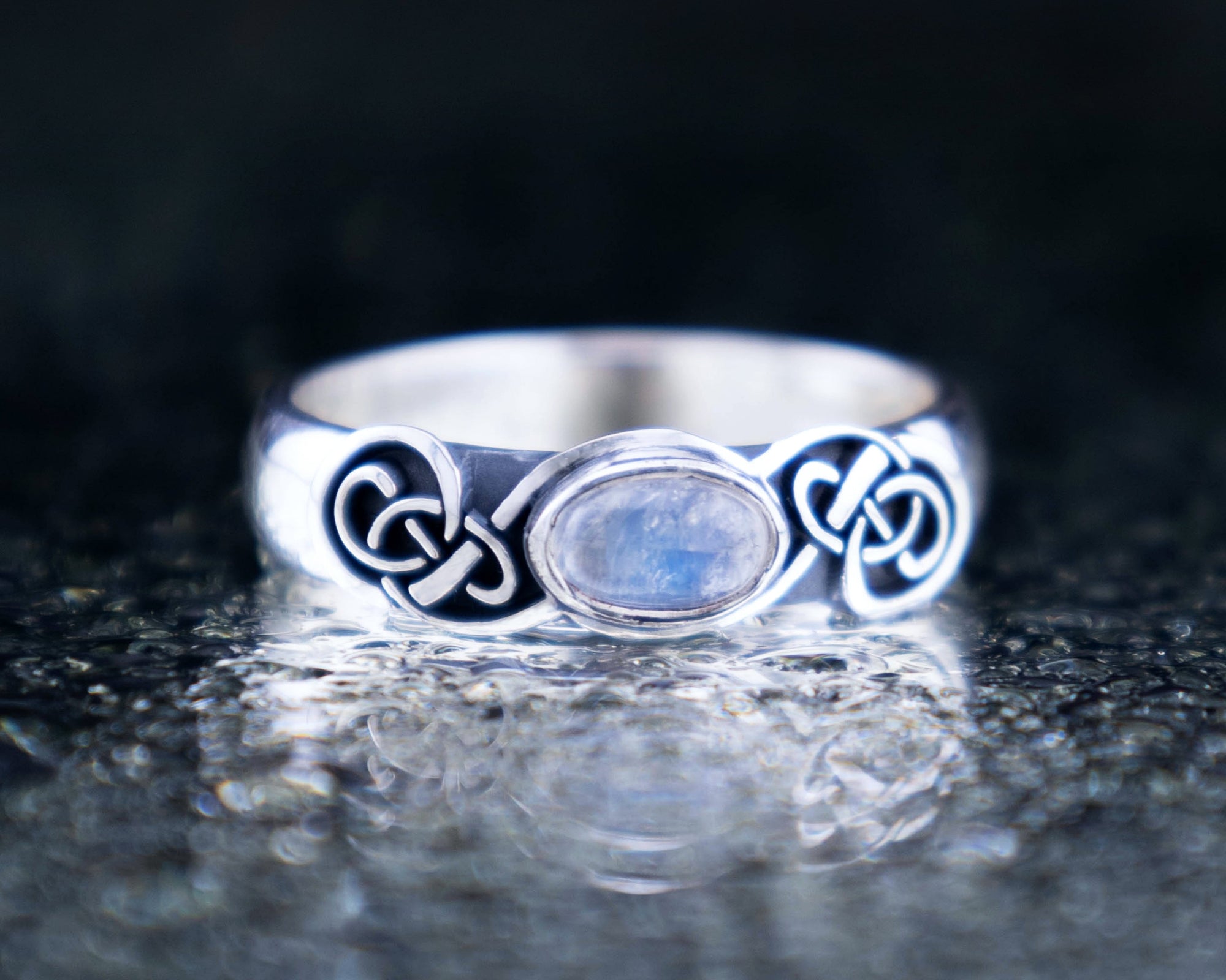 Sterling silver Celtic knot ring with blue labradorite gemstone, oxidized symmetrical knotwork pattern, handmade pagan jewelry on stone surface