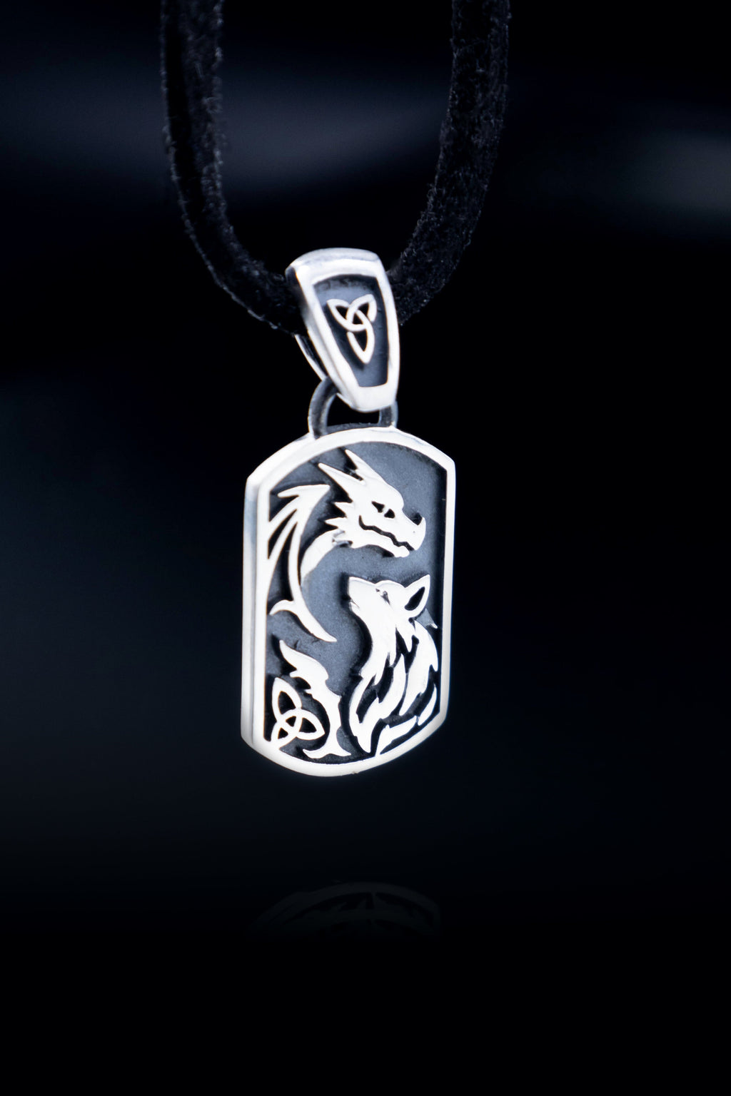 Sterling silver dragon and wolf pendant hanging on black cord against black background, full detail view of raised design and oxidized finish