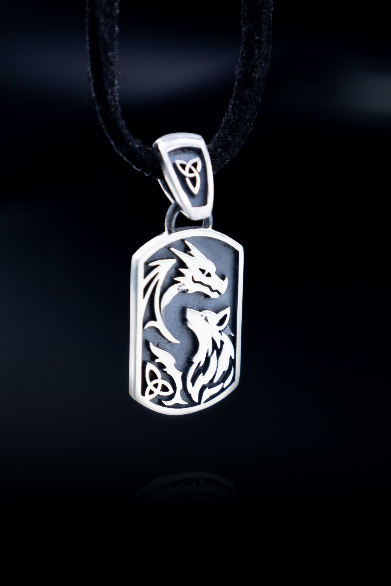 Sterling silver dragon and wolf pendant hanging on black cord against black background, full detail view of raised design and oxidized finish