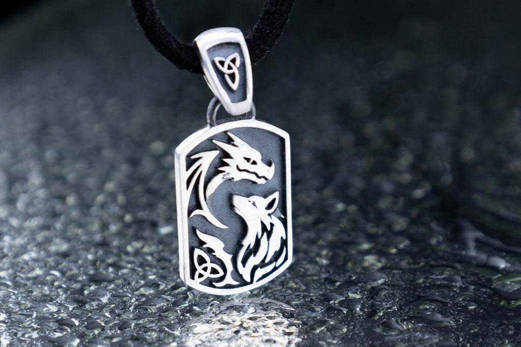Silver pendant with dragon and wolf design on a dark surface