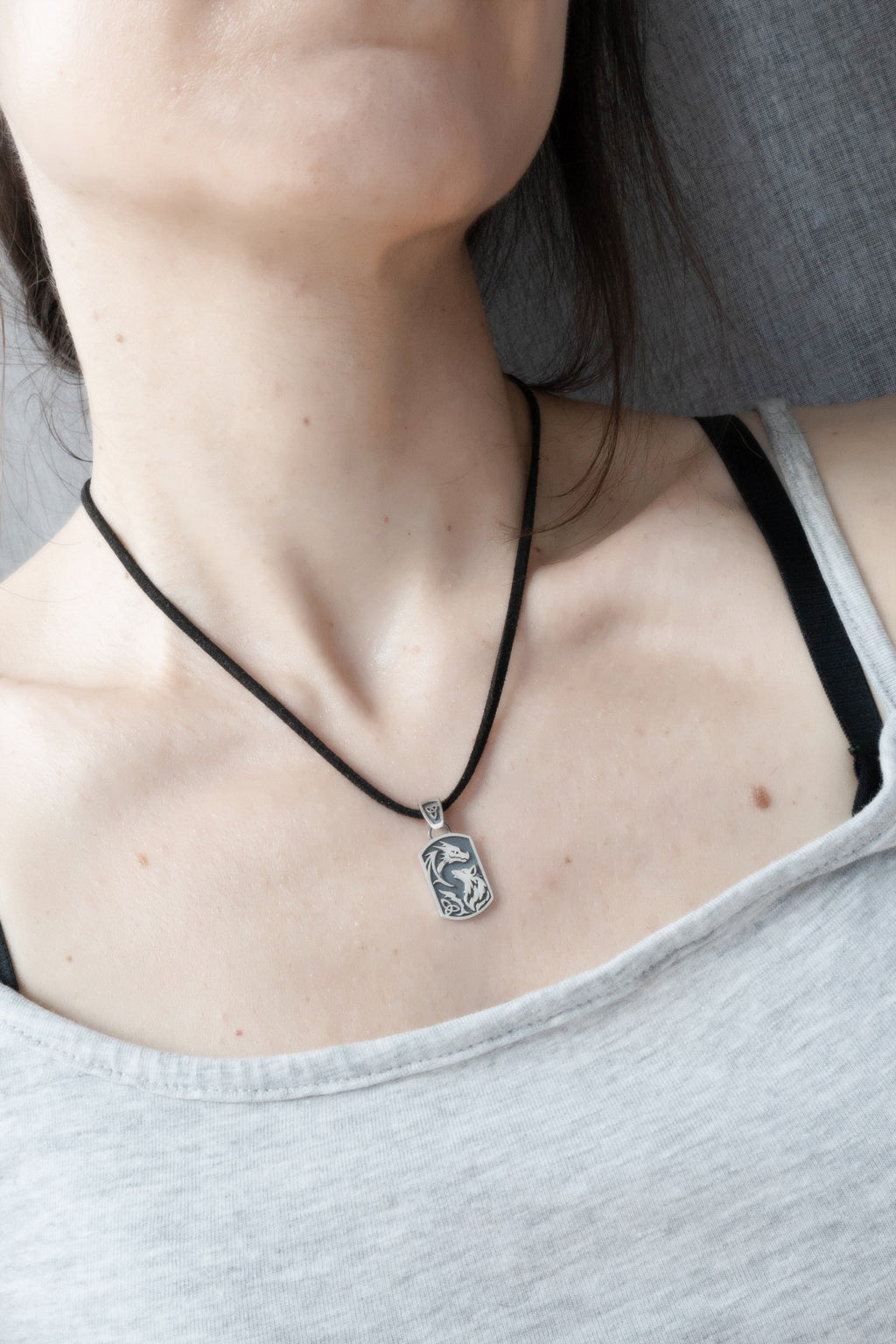 Dragon wolf silver pendant worn on collarbone on black cord, lifestyle jewelry shot, dark fantasy aesthetic