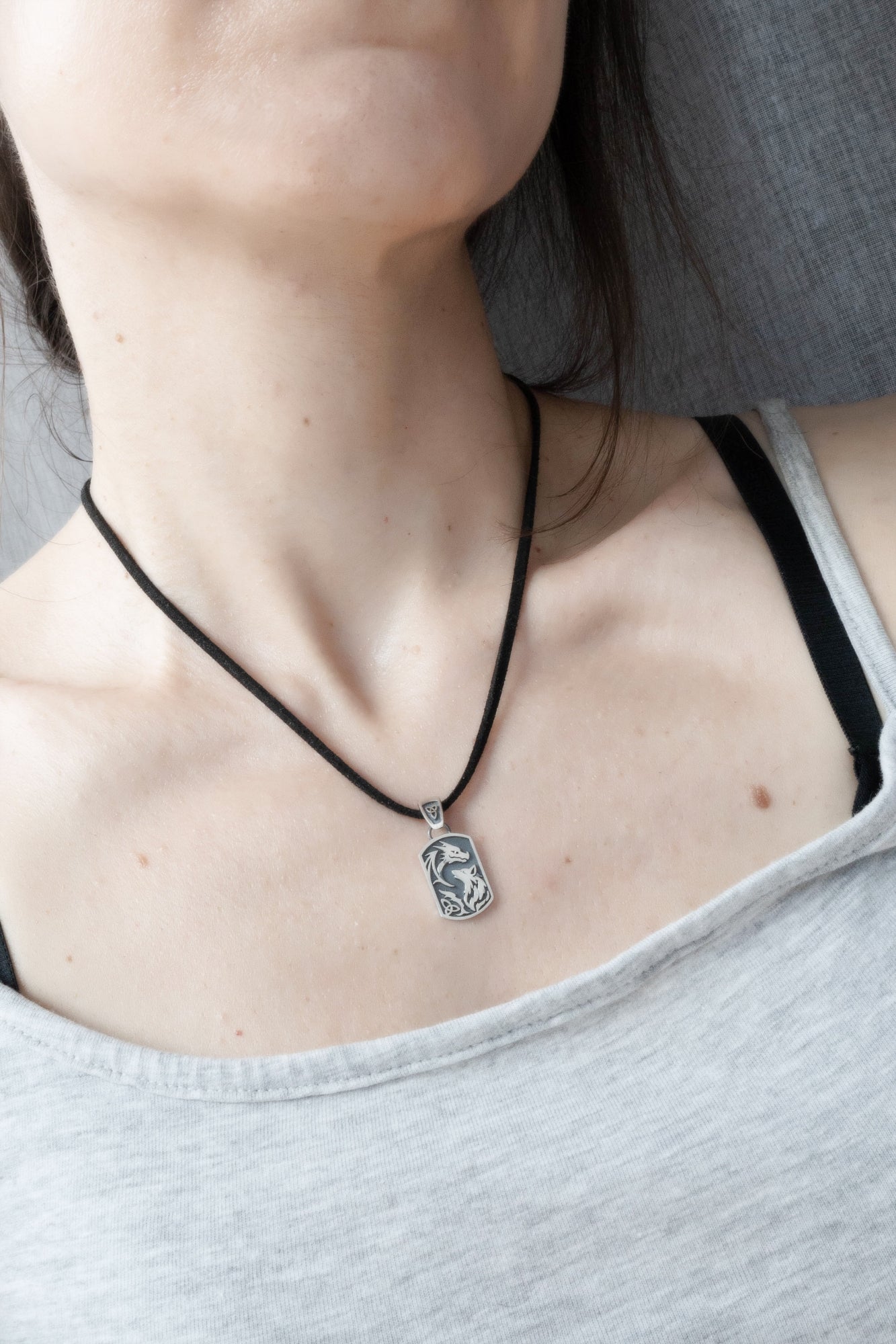 Dragon wolf silver pendant worn on collarbone on black cord, lifestyle jewelry shot, dark fantasy aesthetic