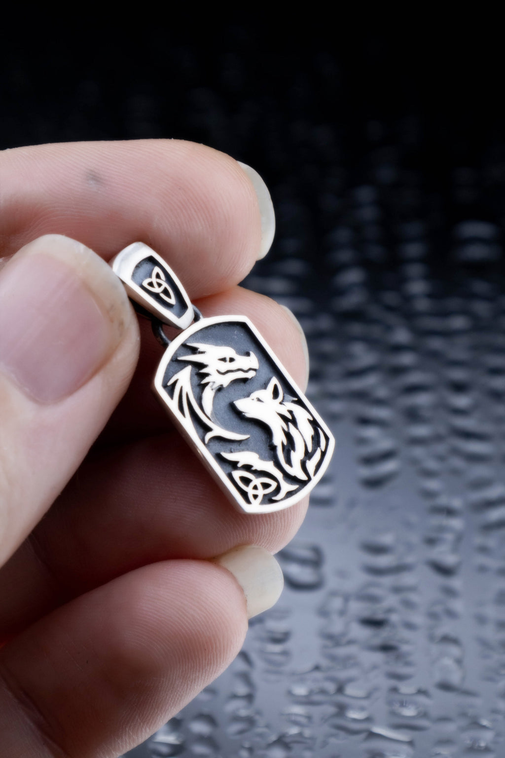 Handmade 925 sterling silver dragon and wolf pendant held in palm, Celtic triquetra bail visible, oxidized dark background