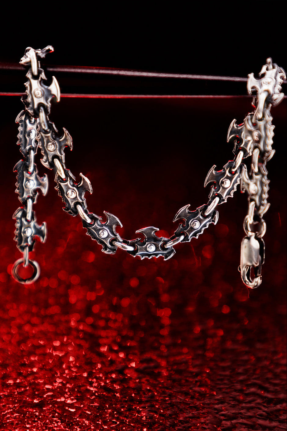 Gothic oxidized silver chainsaw chain bracelet hanging against dark red background