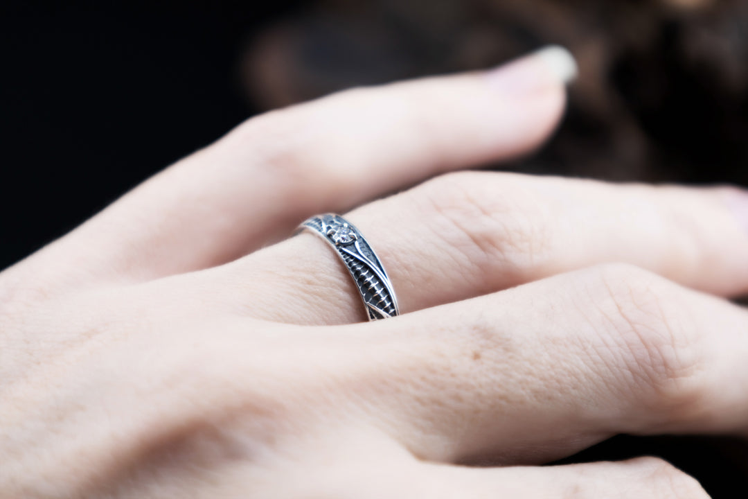 Biomechanical sterling silver ring worn on a finger, showing its slim proportions, asymmetric ribbed pattern and small round lab-grown diamond.