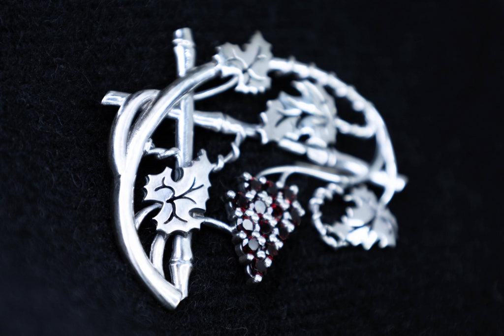 Close-up of sterling silver grape leaves and garnet cluster brooch