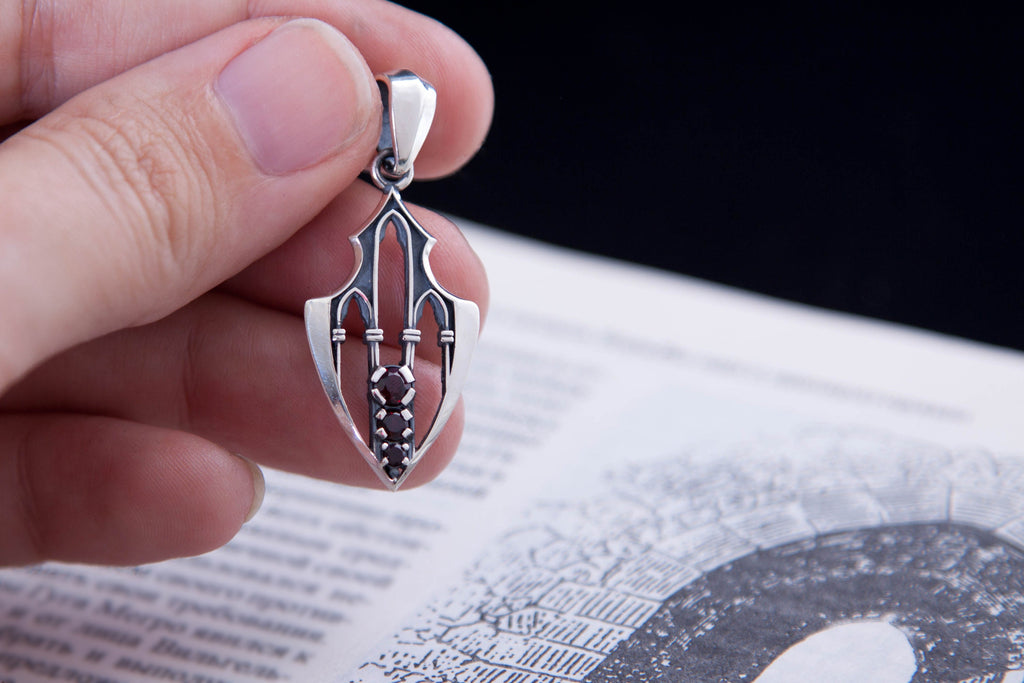Hand holding silver gothic pendant with garnet accents